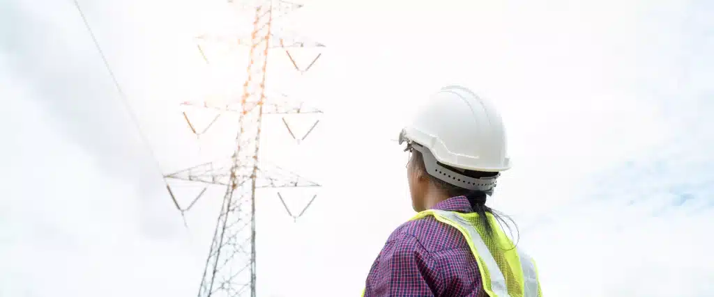 pessoa com capacete e colete de segurança olhando para uma torre elétrica