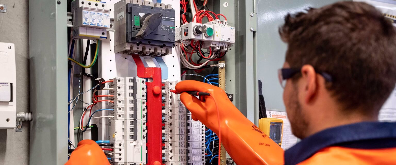 Técnico ajustando painel elétrico com luvas de proteção.